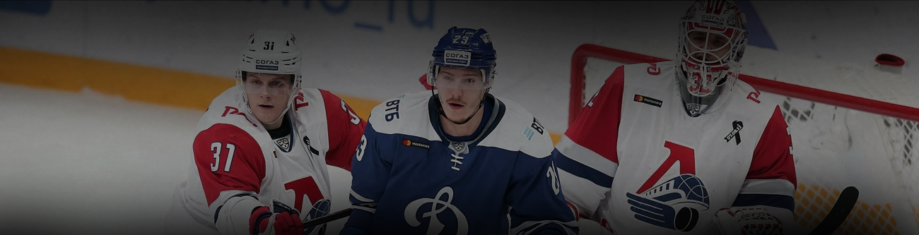 Хоккейный матч: два игрока в бело-красной форме и один в синей форме на льду перед воротами. За ними вратарь в бело-красной форме с логотипом на форме. Игроки сосредоточены, всё в движении